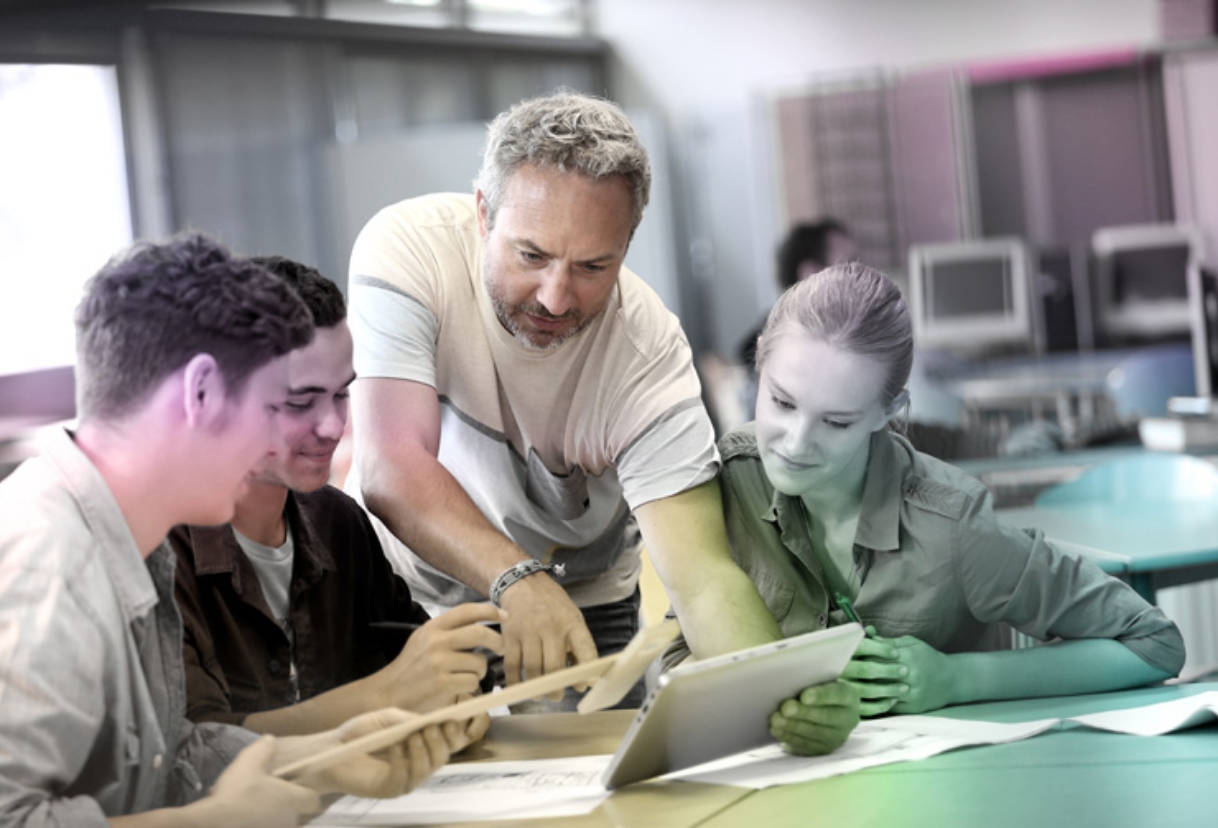 Un enseignant accompagne un groupe d’étudiants dans leur travail sur tablette.
