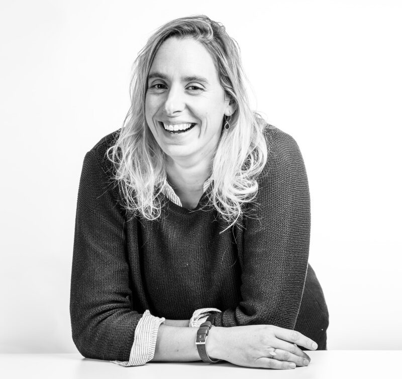 Portrait en noir et blanc d’une femme souriante, assise à une table.